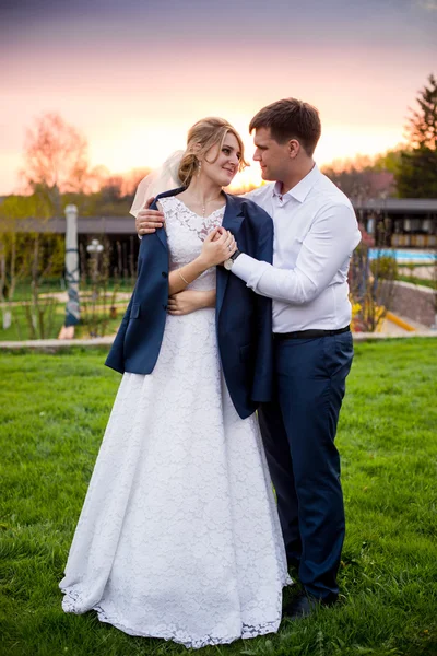 Groom putting jacket on brides shoulder at sunset in park — Stock Photo, Image