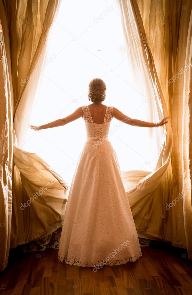 Toned shot of beautiful bride posing at window in hotel room