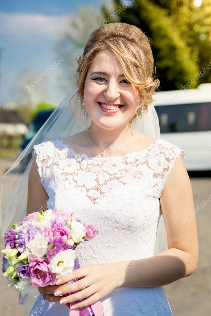 portrait of smiling bride posing in park with wedding bouquet