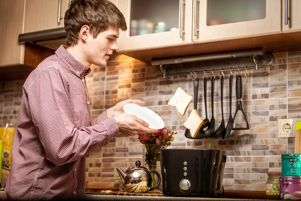 Young man catching fresh popped out toasts on white plate — Stock Photo, Image