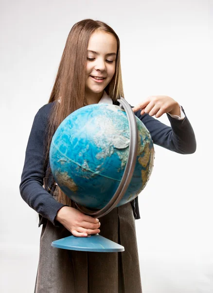 Smiling girl in school uniform pointing at Earth globe — Stock Photo, Image