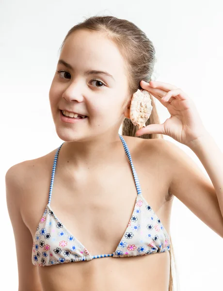 Smiling girl posing with seashell next to ear — Stock Photo, Image