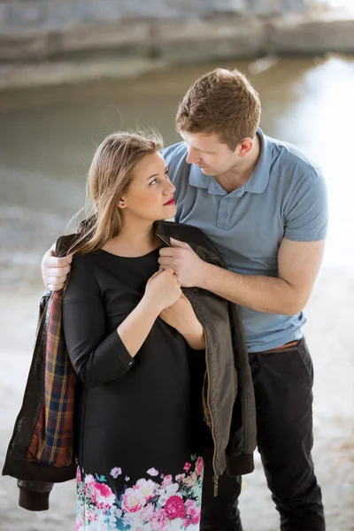 Guapo hombre poniendo chaqueta en novias hombros en riverban — Foto de Stock