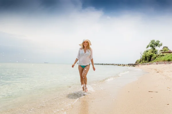 Happy woman in shirt and hat walking in the sea waves on beach — Stock Photo, Image