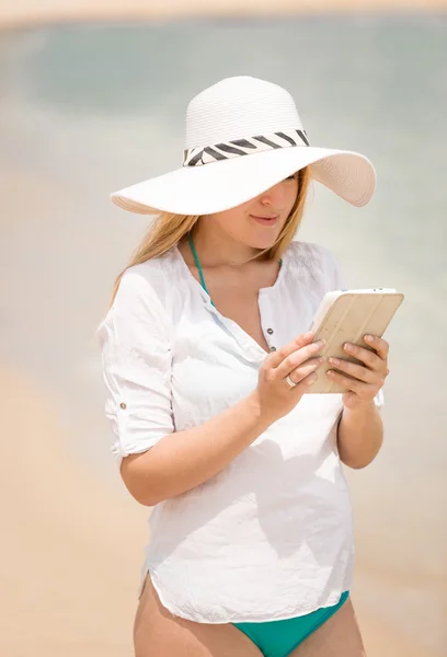 Mujer joven que trabaja en tableta digital en la playa en el día ventoso — Foto de Stock