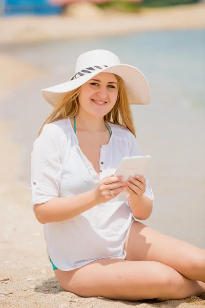 Gelukkige vrouw in hoed poseren met digitale tablet op strand — Stockfoto