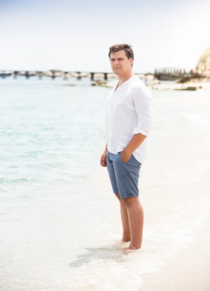 Hombre con estilo en camisa y pantalones cortos de pie en la playa — Foto de Stock
