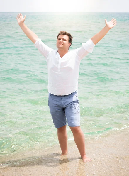 Hombre guapo en camisa disfrutando del mar y levantando las manos en el cielo — Foto de Stock