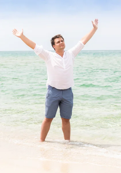 Hombre de pie con las manos en alto en la playa y mirando al cielo — Foto de Stock