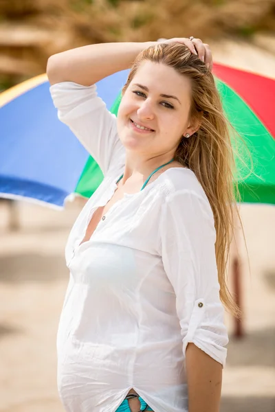 Cute woman in white shirt posing on beach against sun umbrellas — Stock Photo, Image