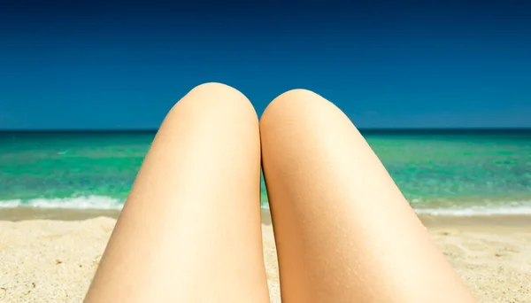 Toned photo of slim female legs tanning on seashore — Stock Photo, Image