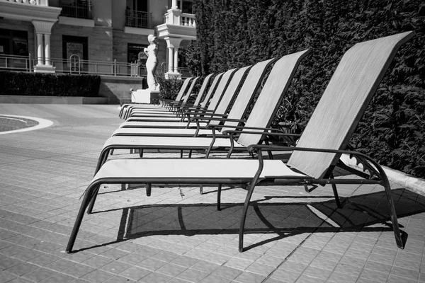 Black and white shot of row of sunbed chairs at pool — Stock Photo, Image
