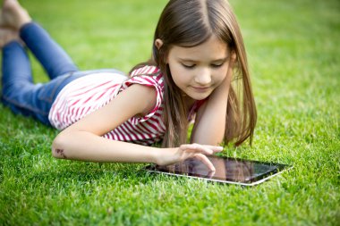 sevimli kız çimlerin üzerine Park'ta dijital tablet kullanma