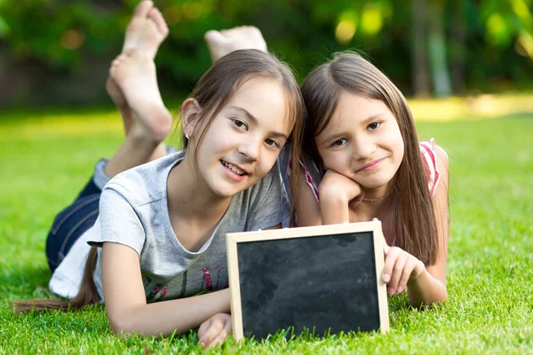 Due bambine in posa su erba con lavagna bianca — Foto Stock