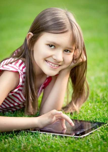 Retrato de linda chica sonriente tumbada en la hierba con tableta digital —  Fotos de Stock