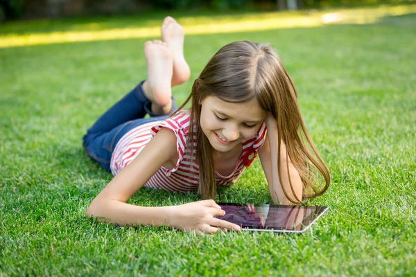 Chica acostada en la hierba y el uso de tabletas —  Fotos de Stock