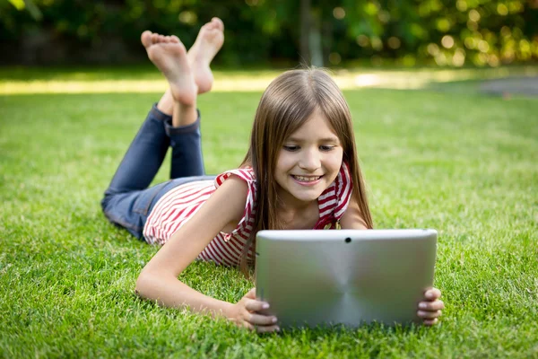 Gelukkig kind liggen op gras met digitale tablet — Stockfoto