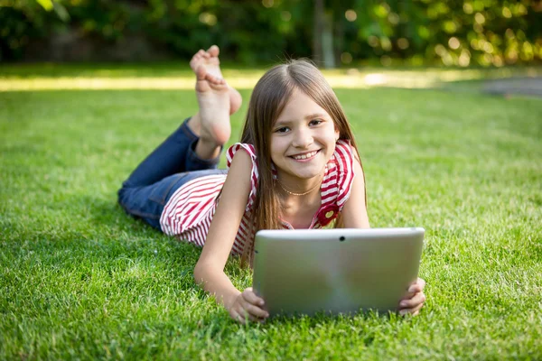 Menina morena relaxante no parque de grama e segurando tablet digital — Fotografia de Stock