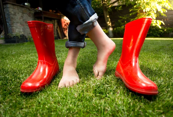 Gros plan de pieds nus fille debout sur l'herbe avec des bottes en caoutchouc rouge — Photo