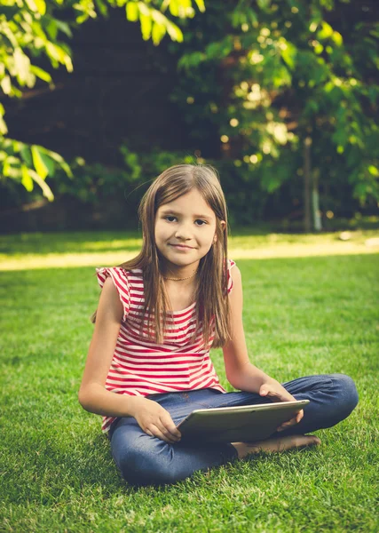 Tónovaný fotografie roztomilá dívka seděla na trávníku a použití digitálních tabulky — Stock fotografie
