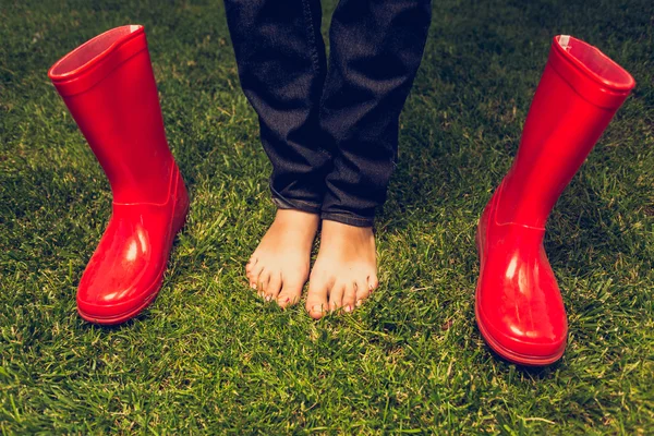 Foto tonificada de chica descalza posando con botas de goma rojas en el prado —  Fotos de Stock