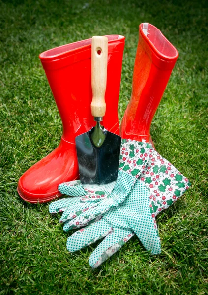 Крупный план лопаты, перчаток и красных резиновых сапог, лежащих на траве — стоковое фото