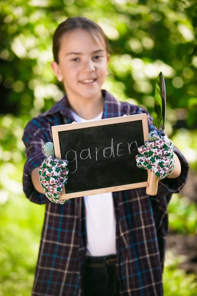 Linda chica en guantes de jardinería sosteniendo pizarra y herramientas — Foto de Stock