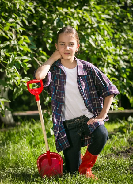 Mädchen in Gummistiefeln posiert mit Spielzeugspaten im Garten — Stockfoto