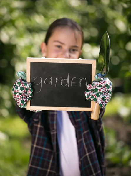 Dziewczynka gospodarstwa tablica z tekstem "ogród" pod choinką — Zdjęcie stockowe