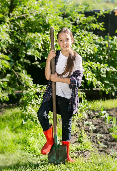 Lächelndes Mädchen in roten Gummistiefeln, das im Garten Erde schaufelt — Stockfoto