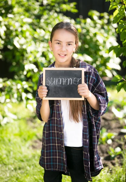 Šťastná dívka pózuje v zahradě s tabulí s slovo "letní" — Stock fotografie