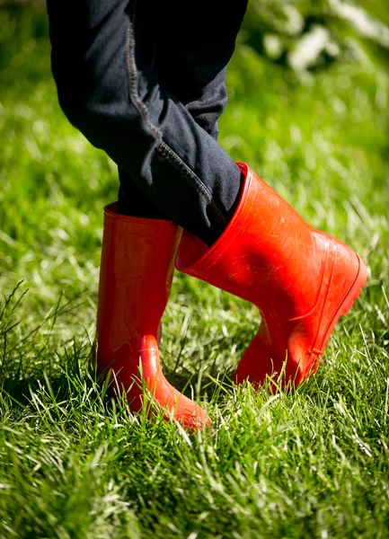 Fechar-se de menina em botas de borracha vermelha posando na grama verde fresca — Fotografia de Stock