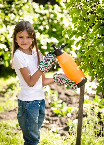 Leende flicka bespruta små äppelträd med gödselmedel — Stockfoto