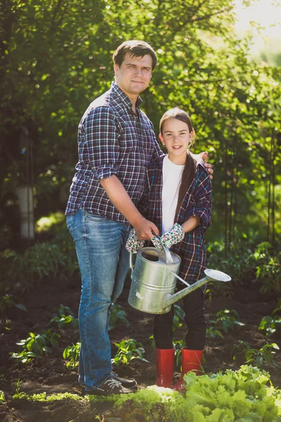 smiling father watering garden with little daughter