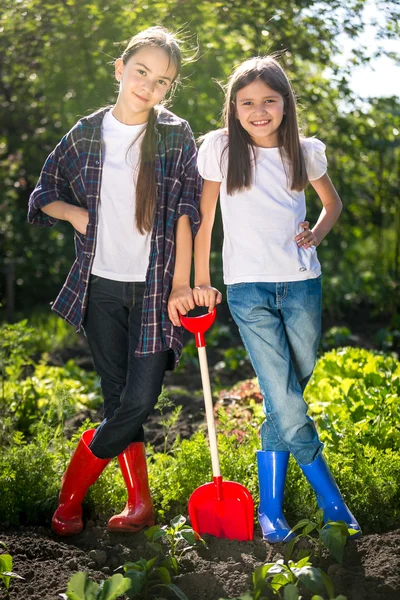 Zwei Mädchen in Gummistiefeln posieren mit Schaufel auf Gartenbeet — Stockfoto