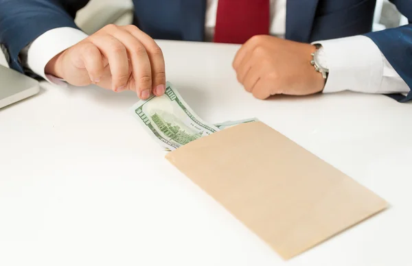Geschäftsmann zieht Geldschein aus Umschlag, der auf Tisch liegt — Stockfoto