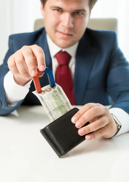 Greedy businessman pulling money out wallet with use of magnet — Stock Photo, Image