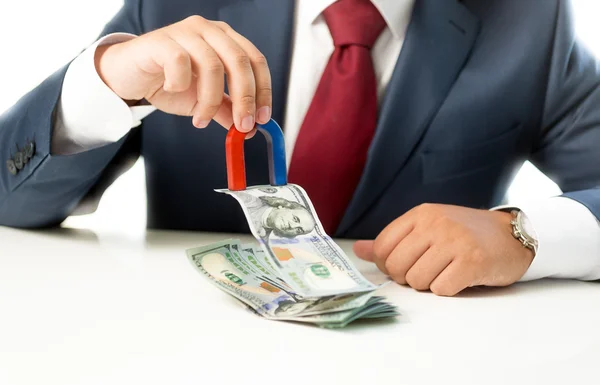 Geschäftsmann zieht mit Magnet Geld aus Stapel auf Tisch — Stockfoto