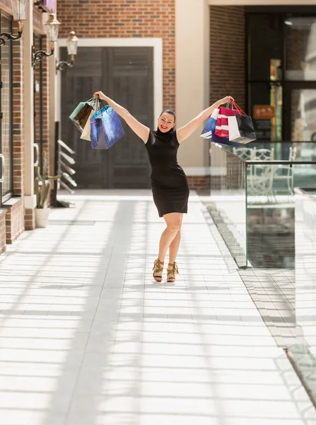 Mulher sorrindo posando com sacos de papel no shopping — Fotografia de Stock