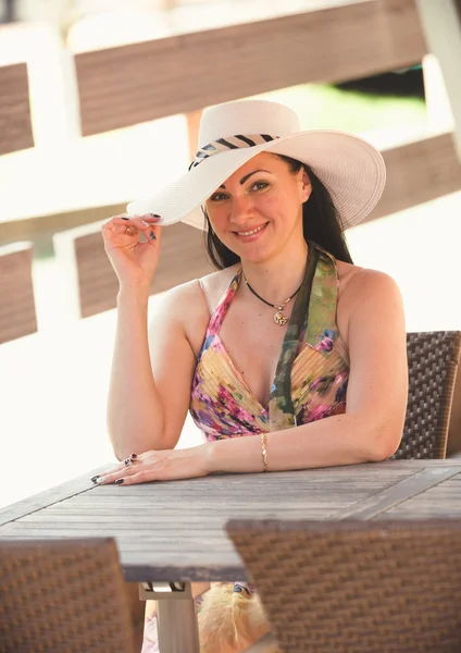 Portrait of happy woman in hat posing at cafe behind table — Stock Photo, Image