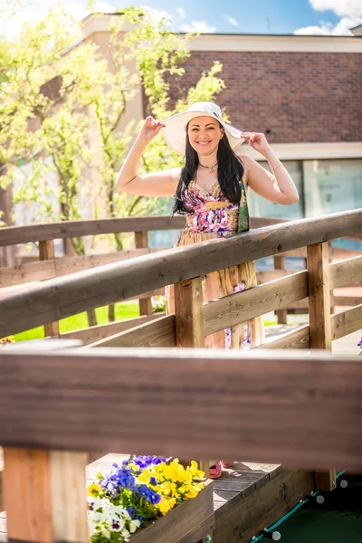 Lachende vrouw in hoed wandelen over de houten brug op zonnige dag — Stockfoto