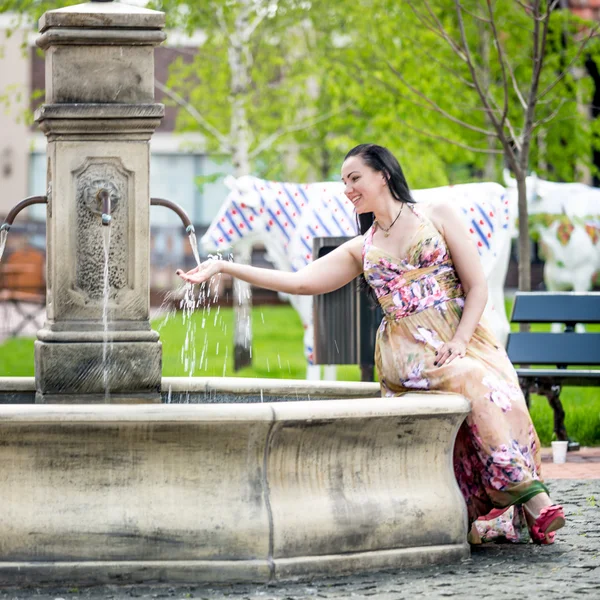 Woman sitting on side of fountain and holding hand under water — Stock Photo, Image