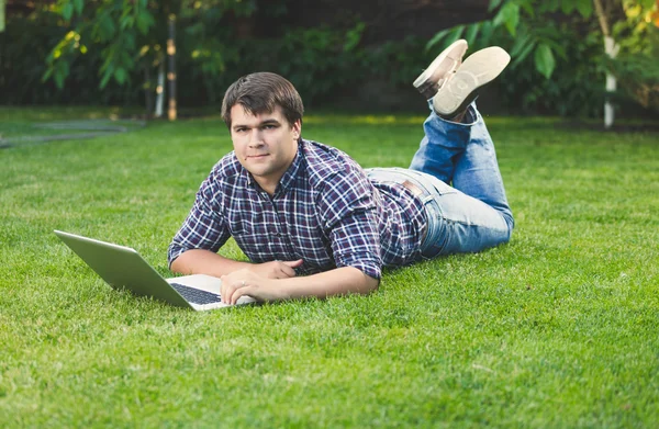 Young man lying on grass at park and working with laptop — Stock Photo, Image