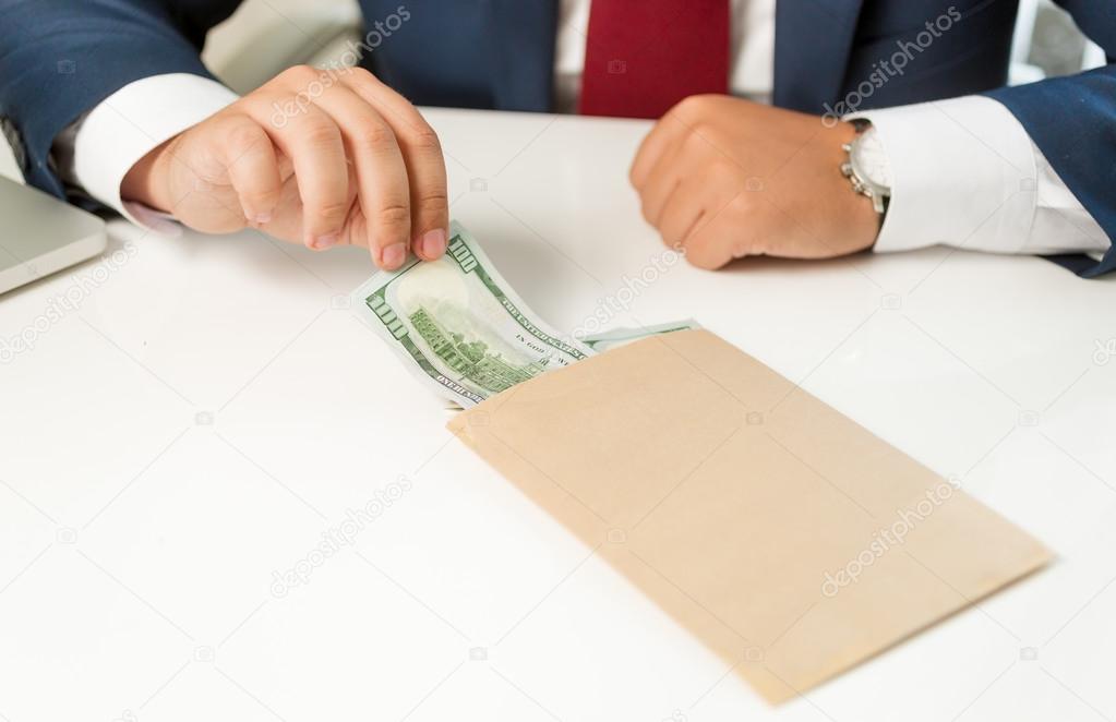 businessman pulling banknote out of envelope lying on table