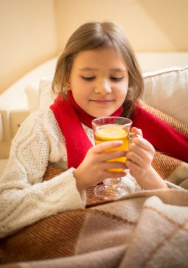 cute girl lying in bed and holding cup of tea with lemon
