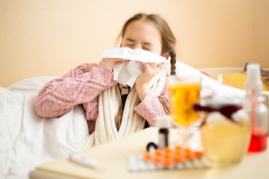 little girl lying in bed and blowing nose in paper handkerchief