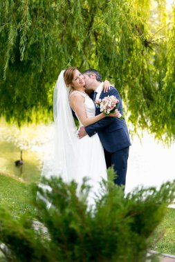 Beautiful bride and groom passionately kissing under tree