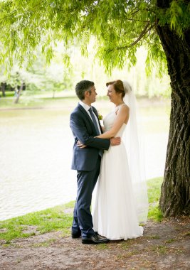 bride with long hugging with groom under big tree at park