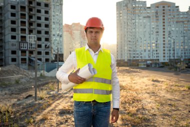 Portrait of engineer posing with blueprints against building sit