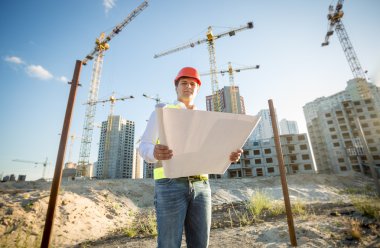 engineer in hardhat inspecting blueprints on building site